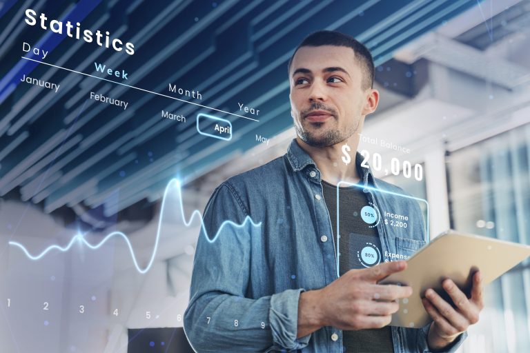 A young man holding a digital tablet and analyzing financial data visualized through an augmented reality interface, showing monthly statistics, income and expense ratios, and a total balance of $20,000, representing the rise of fintechs and their impact on personal finance management in the digital age.