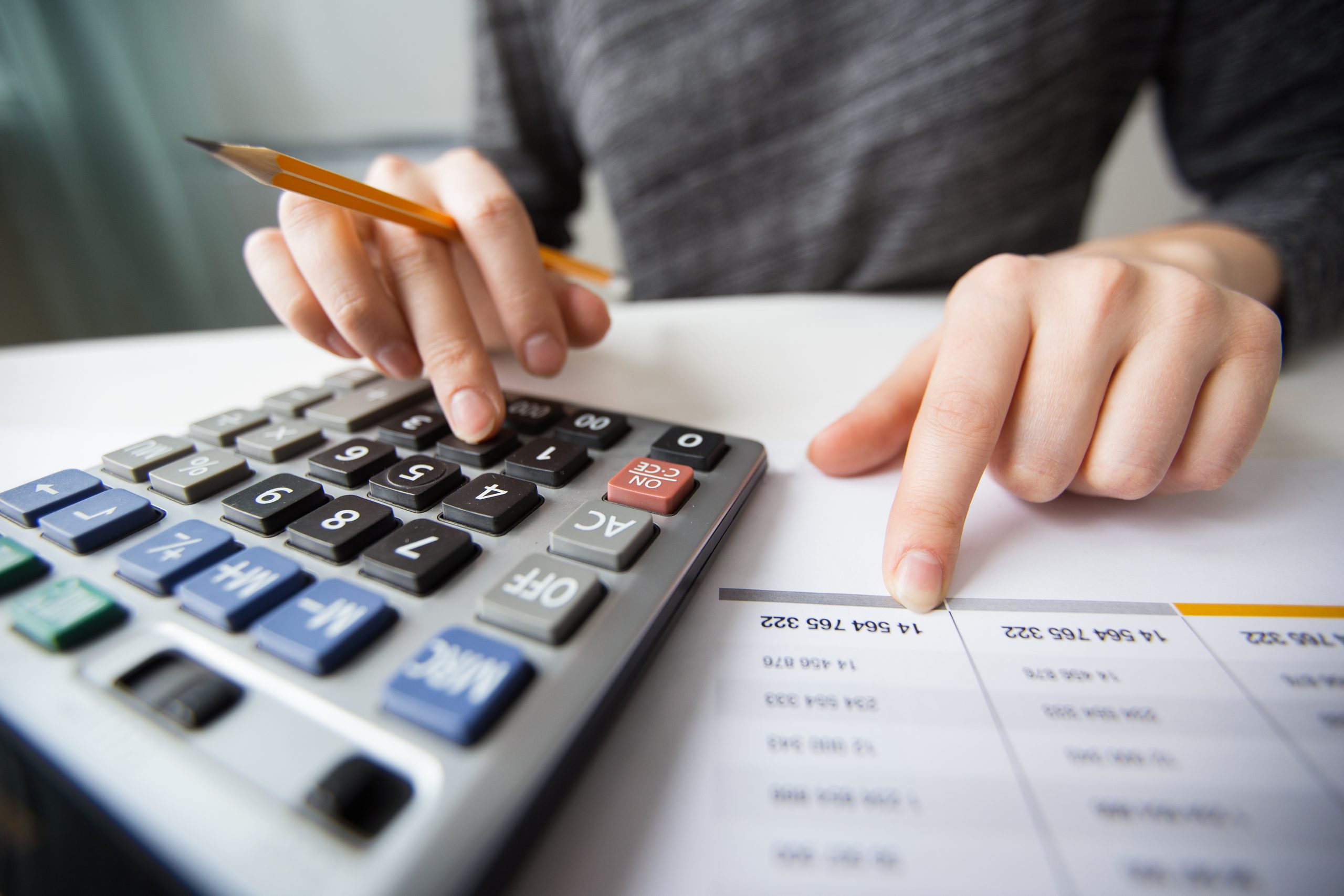 A person calculating financial data using a large calculator while reviewing printed figures related to trade tariffs, emphasizing economic analysis and fiscal decision-making.