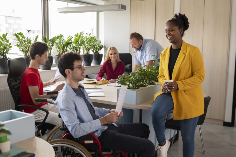 A diverse group of professionals, including a person in a wheelchair and individuals of different ethnicities and genders, collaborating in a modern office space filled with plants. This inclusive environment reflects the values of financial inclusion and equal opportunity in the workplace.