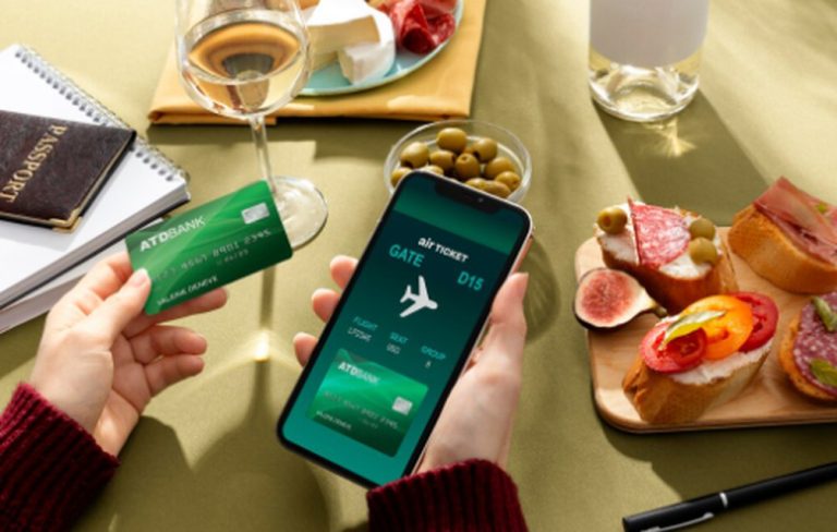 A person holding a green bank card and a smartphone displaying a digital boarding pass, surrounded by wine, snacks, and travel essentials, illustrating the comfort provided by credit cards with airport lounge access.
