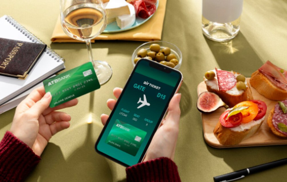 A person holding a green bank card and a smartphone displaying a digital boarding pass, surrounded by wine, snacks, and travel essentials, illustrating the comfort provided by credit cards with airport lounge access.