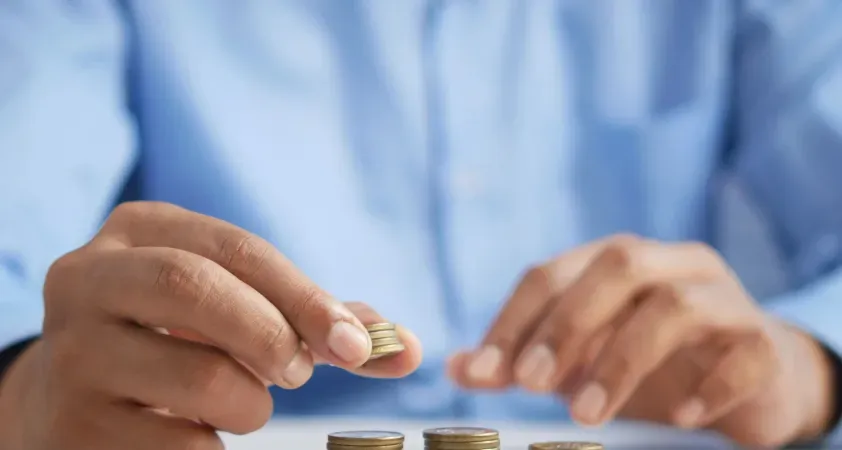 Man counting coins on a table, symbolizing financial planning, saving, and personal money management.