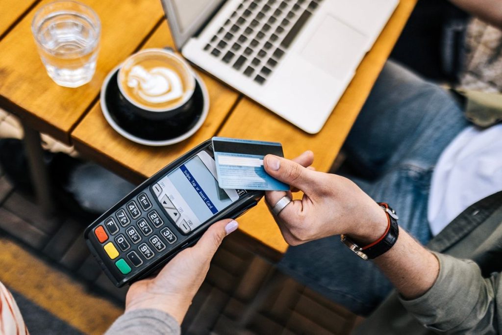 A person paying for coffee with a credit card at a café, illustrating the everyday convenience and rewards of using the best cashback credit cards with no annual fee.
