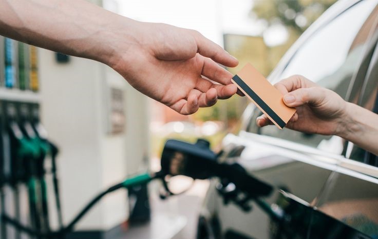 A person handing a credit card at a gas station, representing the savings and rewards earned by using the best cashback credit cards with no annual fee for fuel purchases.