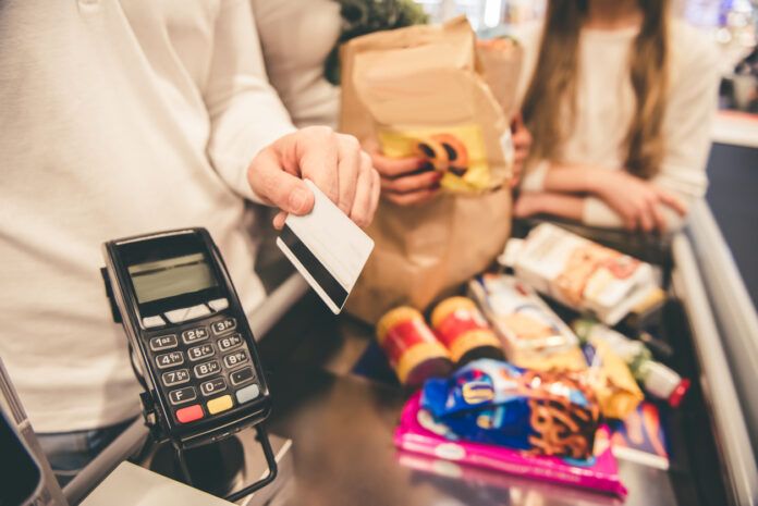 A shopper paying for groceries with a credit card at the checkout, highlighting the everyday benefits of using the best cashback credit cards with no annual fee for supermarket purchases.