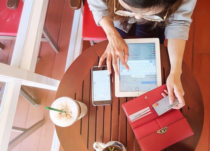 A woman shopping online using a tablet and credit card at a café, illustrating the convenience and savings of the best cashback credit cards with no annual fee for digital purchases.