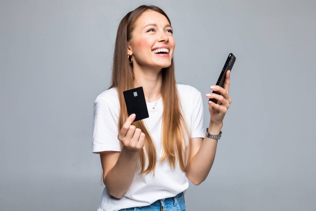 Smiling young woman holding a credit card and a smartphone, representing confidence in choosing the best credit cards for beginners 2025.