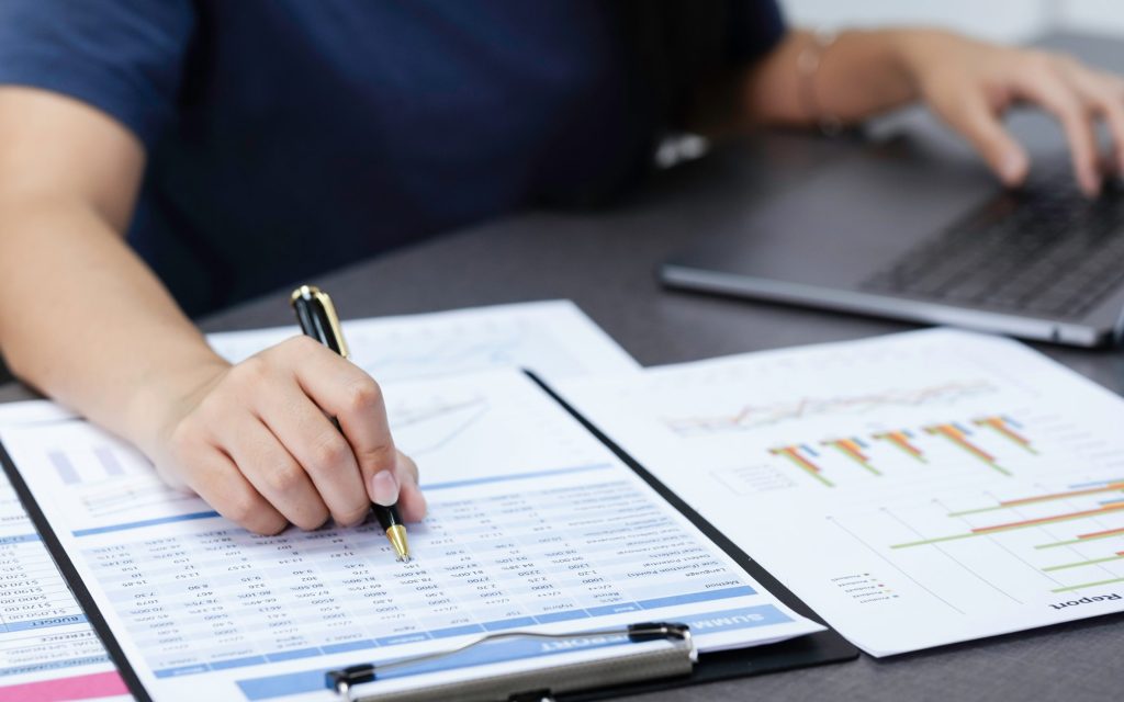 How to pay off debt in 2025: Person analyzing financial spreadsheets and charts on a desk with a laptop in the background, symbolizing planning to pay off debt in 2025.