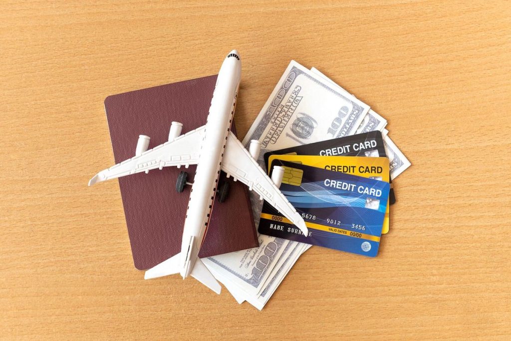 Miniature airplane resting on a passport, U.S. dollar bills, and several credit cards on a wooden table — symbolizing travel, expenses, and the best travel credit cards for earning rewards and perks.