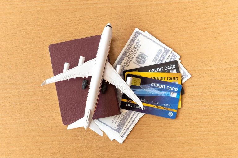 Miniature airplane resting on a passport, U.S. dollar bills, and several credit cards on a wooden table — symbolizing travel, expenses, and the best travel credit cards for earning rewards and perks.