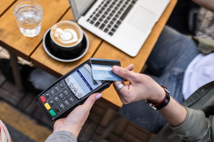 Person paying for coffee at a café using a credit card on a card reader, symbolizing everyday spending and how the best travel credit cards help earn points and travel rewards.