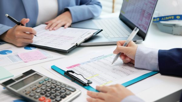 People reviewing financial documents with calculators and a laptop at a desk, illustrating practical steps on how to create a monthly budget that works for managing expenses and saving money.