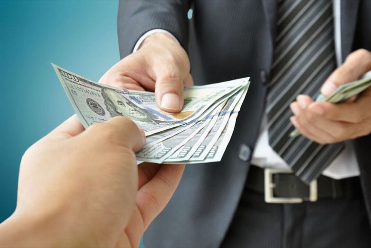 A person handing cash to another individual, representing practical steps on how to stop living paycheck to paycheck by taking control of money and financial decisions.