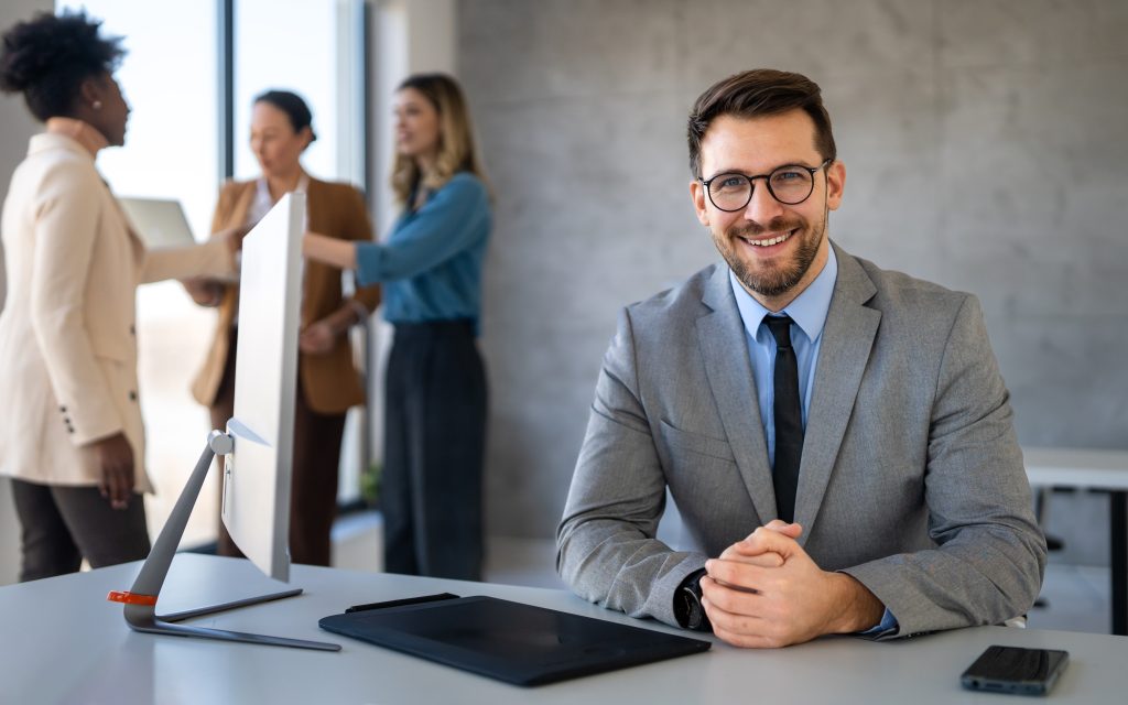 Professional smiling at desk in modern office while colleagues discuss in background, illustrating how to switch banks hassle free with confidence and planning.